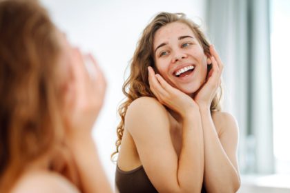 Close-up of a young woman looking at pimples in the mirror. Red spots, rash, acne. Skin treatment.