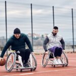 Happy men with disabilities playing basketball on outdoor sports court.