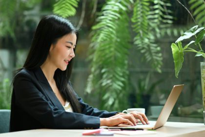 Smiling millennial businesswoman using laptop computer in green eco friendly working space.